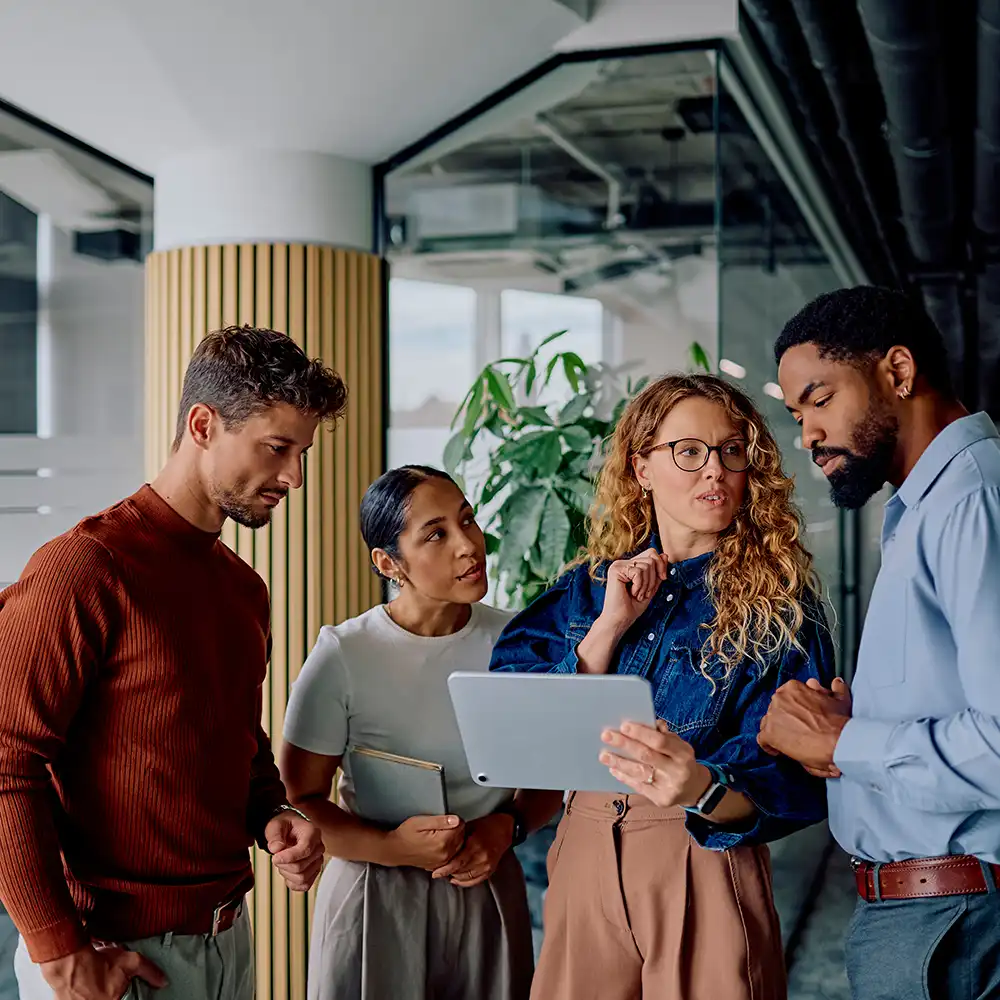 Vielfältiges Geschäftsteam arbeitet zusammen, bespricht Projekt auf einem Tablet in einem modernen Büro und zeigt Teamwork und Problemlösungskompetenz.