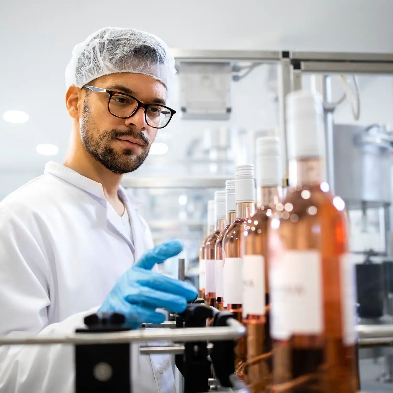 Techniker in weißer Kleidung und Haarnetz, der die Produktion von Getränken in einer Weinabfüllanlage überwacht.